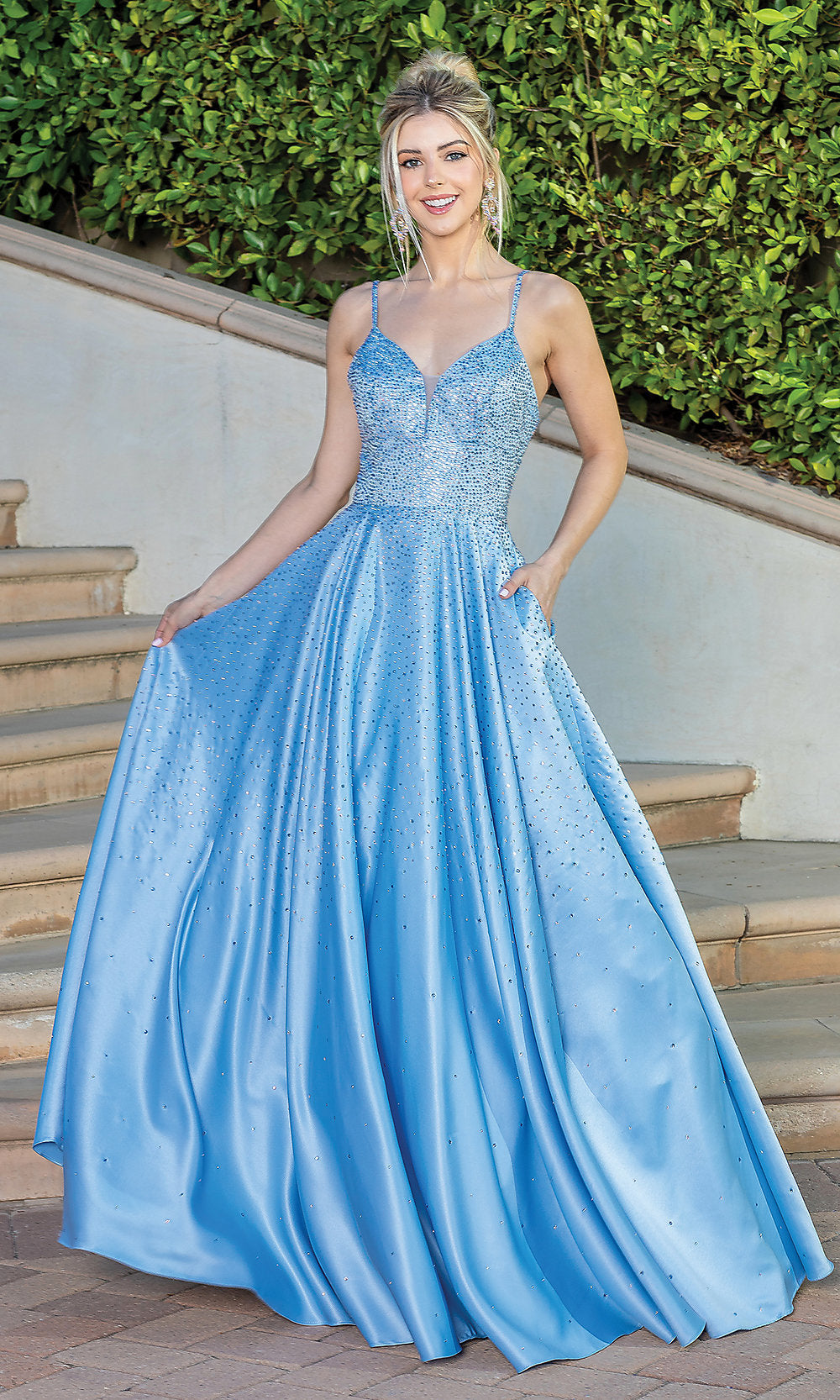 A woman smiles at the camera while standing on outdoor steps, wearing a light blue Corset-Back Long Beaded A-Line Prom Dress with a floor-length v-neckline, thin straps, and pockets.